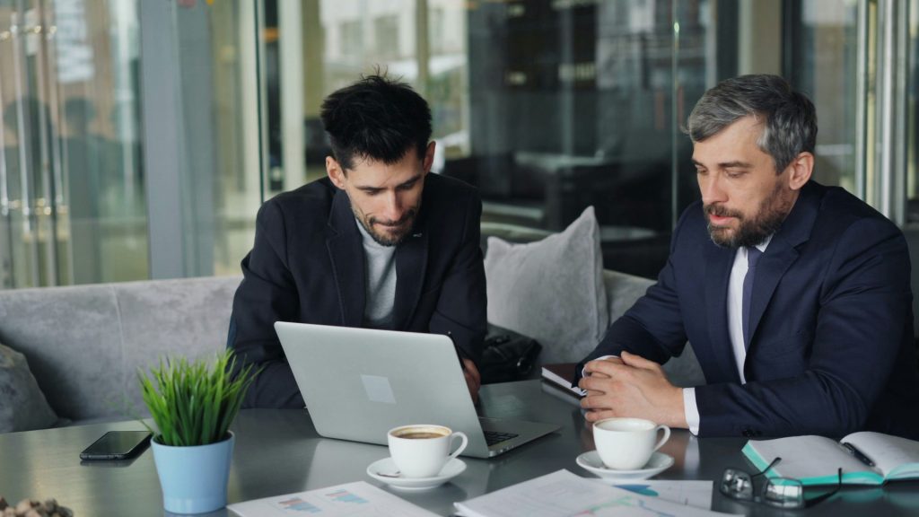 deux hommes assis à une table regardant un ordinateur portable