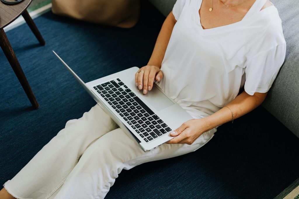 Un adulte assis à l'intérieur utilisant un ordinateur portable sur un sol en moquette bleue, transmettant une ambiance décontractée de travail à domicile.