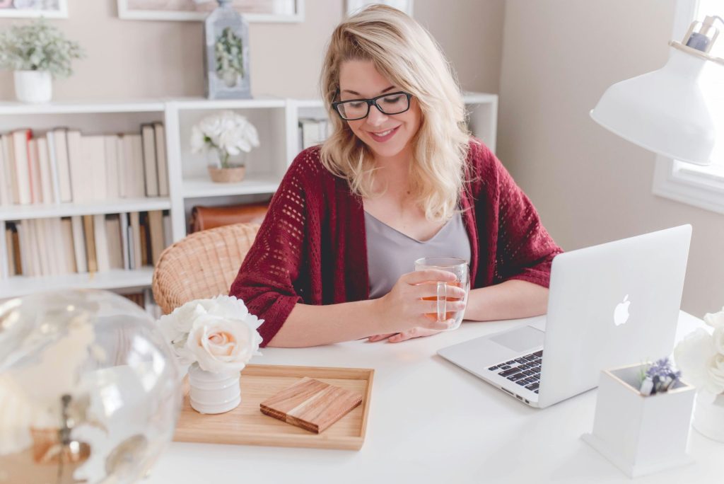 Femme souriante, tenant une tasse en verre, assise à côté d'une table avec un ordinateur portable